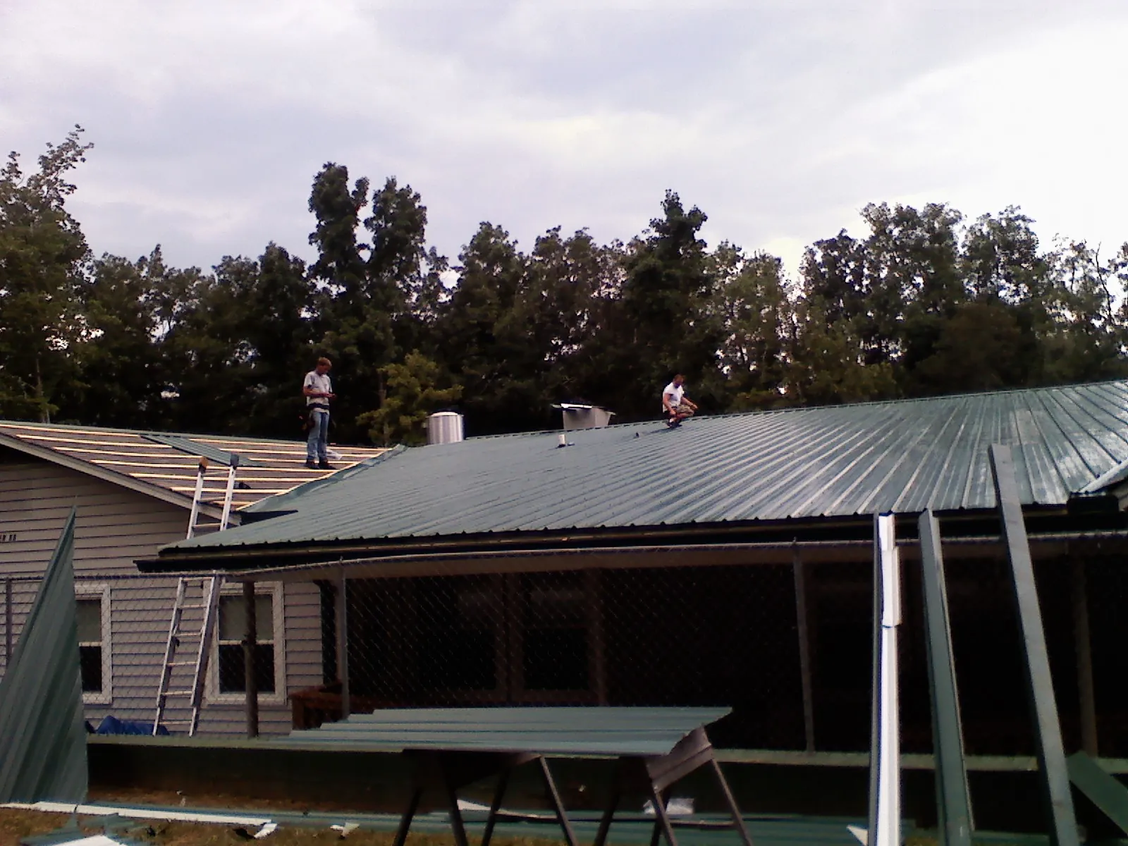 Two roofers installing green metal panels above a covered porch in Norwich