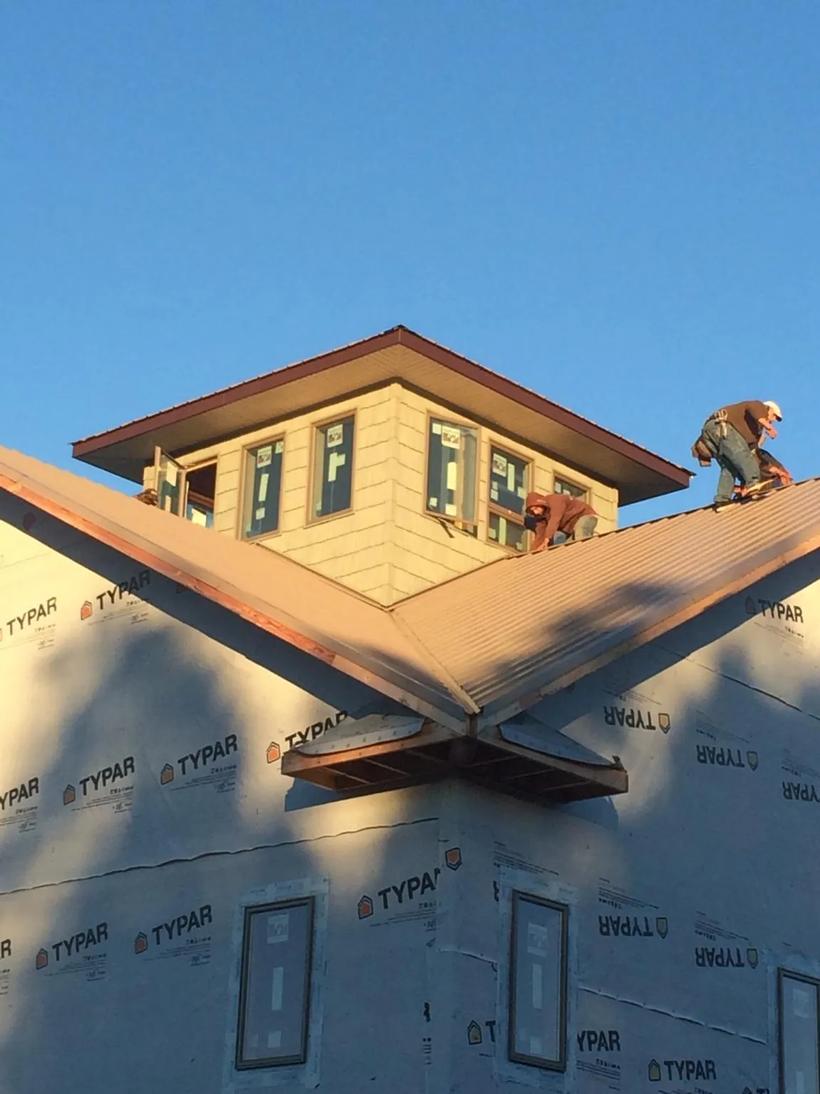 Roofers working around a rooftop cupola on a new metal roof at sunset — Roof Waterproofing in Norwich by Roofing Brothers